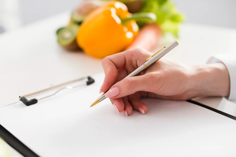 Mão a registar um plano alimentar, com legumes frescos ao fundo