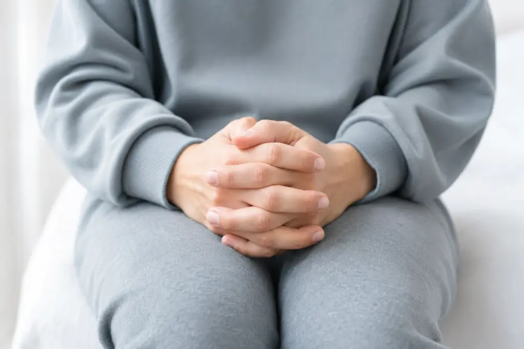 Mãos entrelaçadas sobre os joelhos, em fundo claro